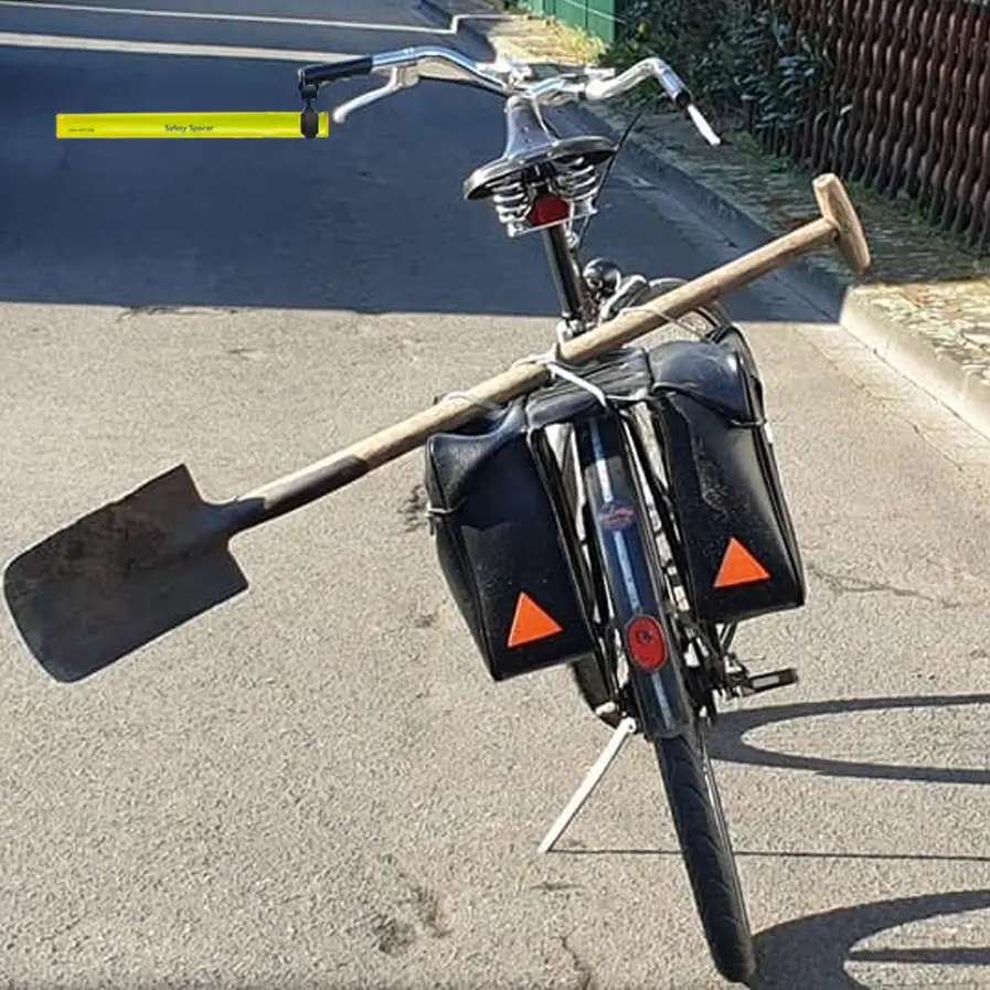 A humorous and creative example of a cyclist using a large spade as a DIY solution to enforce a safe passing distance for cyclists.