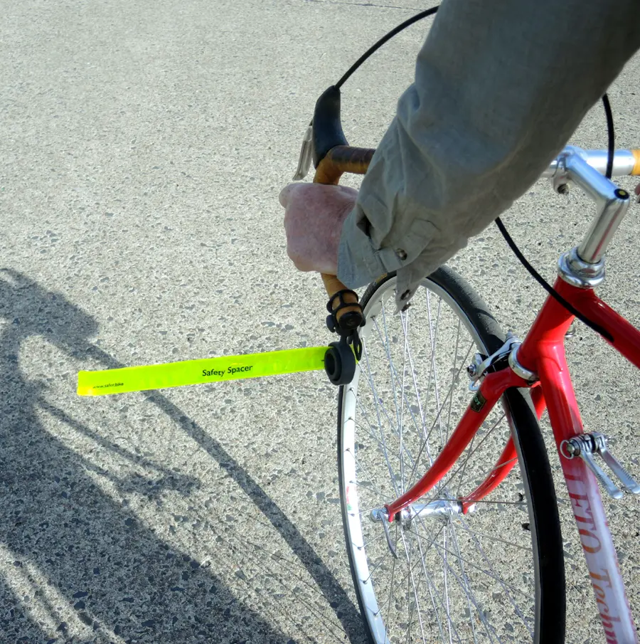 Fahrrad Abstandshalter: Das gestreckte, hochreflektierende Schnappband des Safety Spacers ragt im rechten Winkel vom gebogenen Lenker eines Rennrads in den Raum neben dem Rad und markiert so für überholende Autos den erforderlichen Sicherheitsabstand.