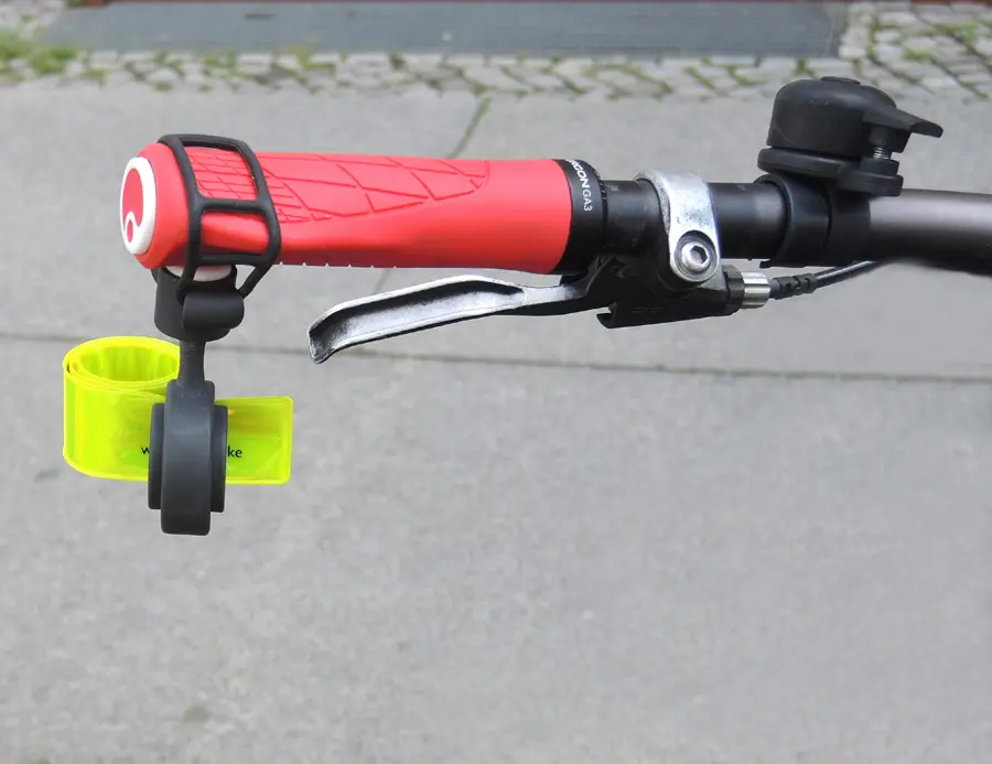 Der Fahrrad Abstandshalter "Safety Spacer" ist an einem roten Fahrradlenkergriff befestigt. Das hochreflektierende gelbe Schnappband ist eingerollt, weil das Fahrrad abgestellt ist. Eingerollt nimmt das Schnappband anderen Fahrräder keinen Platz weg.