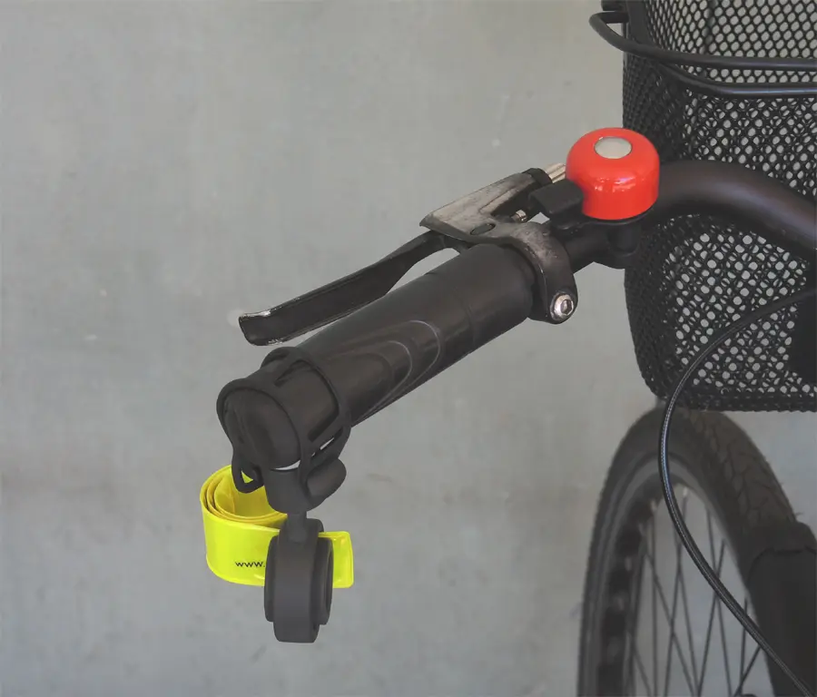 Der am Lenkerende eines geparkten Fahrrads befestigte Safety Spacer Fahrrad Abstandshalter ist platzsparend zusammengerollt. Das eingerollte Schnappband kann jederzeit mit einem Handgriff gestreckt werden, um den erforderlichen Sicherheitsabstand zu signalisieren.