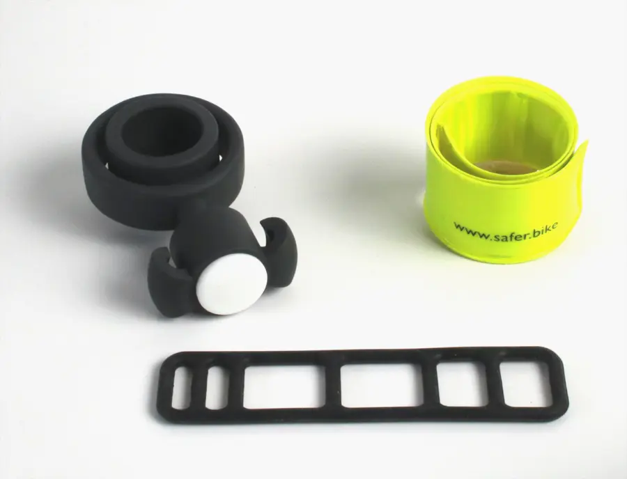 Safety Spacer Fahrrad Abstandshalter Montageanleitung: Die Komponenten des Safety Spacer Sets: die schwarze Halterung für den Lenker, das aufgerollte, hochreflektierende Schnappband und das flexible Silikonband zur Befestigung des Abstandshalters am Lenker..