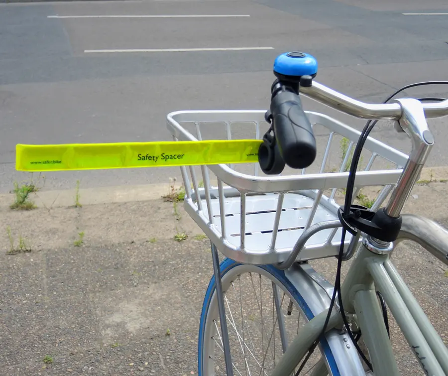 Ein Fahrrad Abstandshalter Safety Spacer ist am Lenker eines Stadtfahrrads mit Korb montiert. Der ausgefahrene Fahrrad Abstandshalter Abstandshalter hilft dabei, den seitlichen Sicherheitsabstand zu wahren.