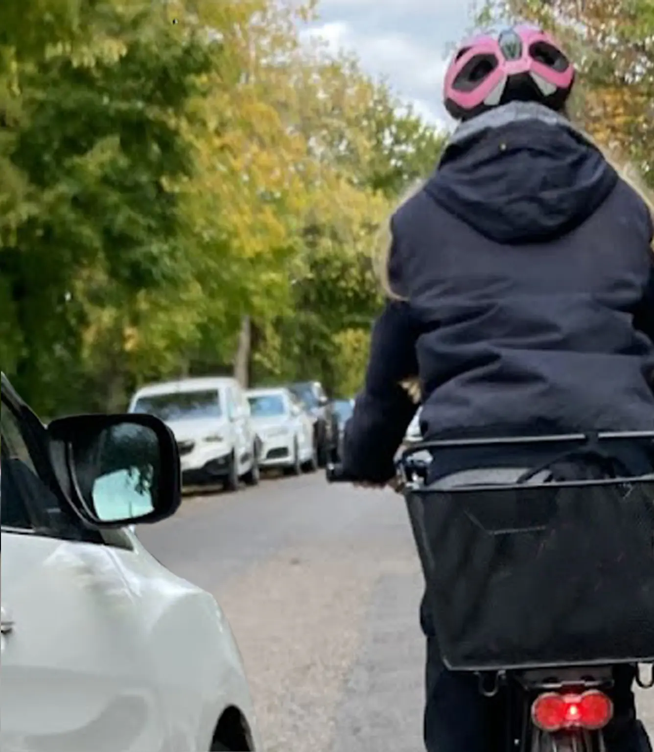 Der Rückspiegel eines Autos berührt beim Überholen einer Radfahrerin fast den Fahrradlenker. Eine Radfahrerin wird auf einer Wohnstraße von einem Auto extrem eng überholt. Der Rückspiegel des Autos berührt fast den Lenker, was die Notwendigkeit für einen ausreichenden Sicherheitsabstand für Radfahrer verdeutlicht. Der Fahrrad Abstandshalter Safety Spacer kann das vermeiden.